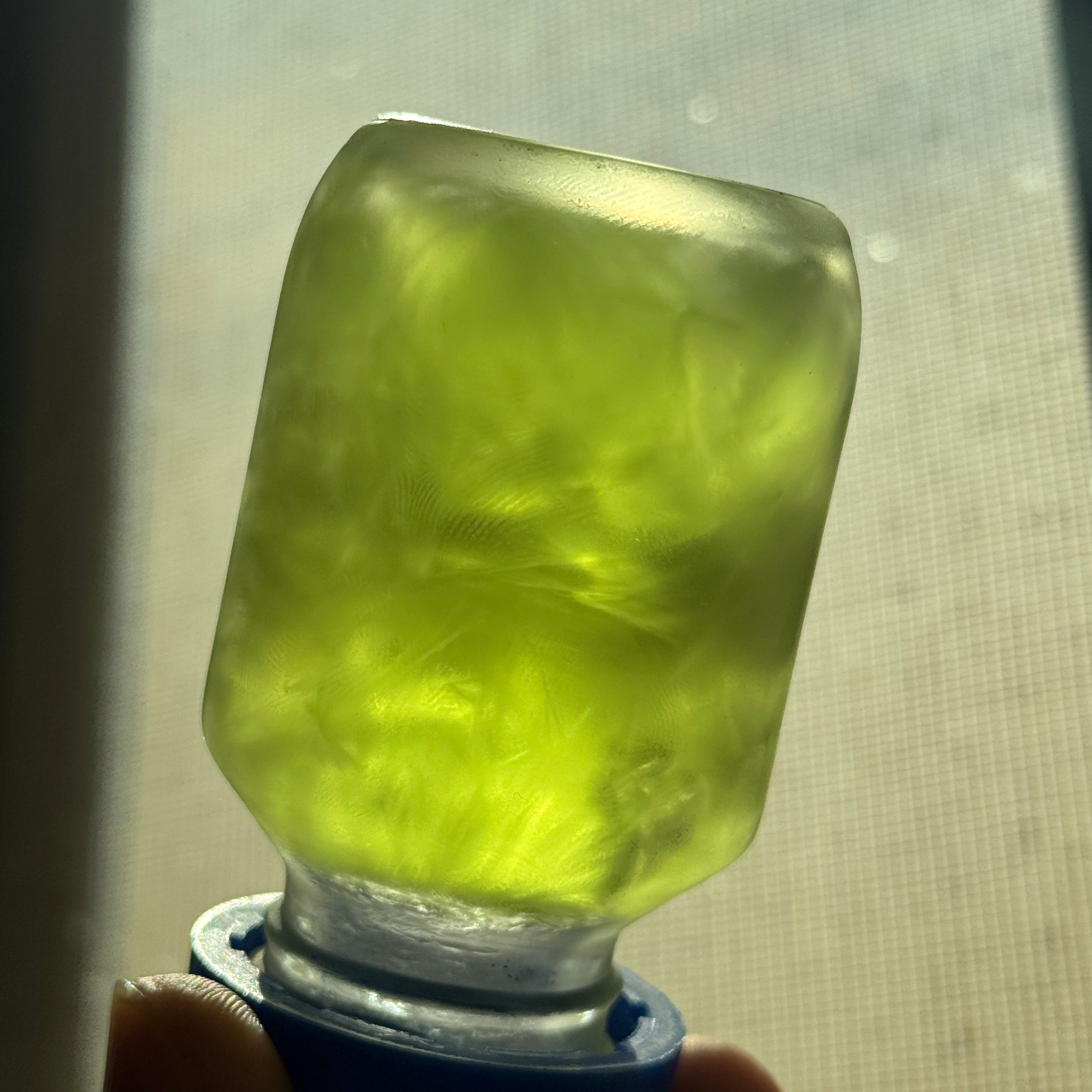 Clear glass bottle with green liquid held by a hand against a metallic surface